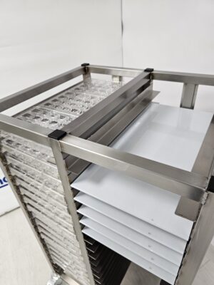 Stainless steel chocolate cooling trolley with multiple trays holding polycarbonate moulds and flat cooling sheets